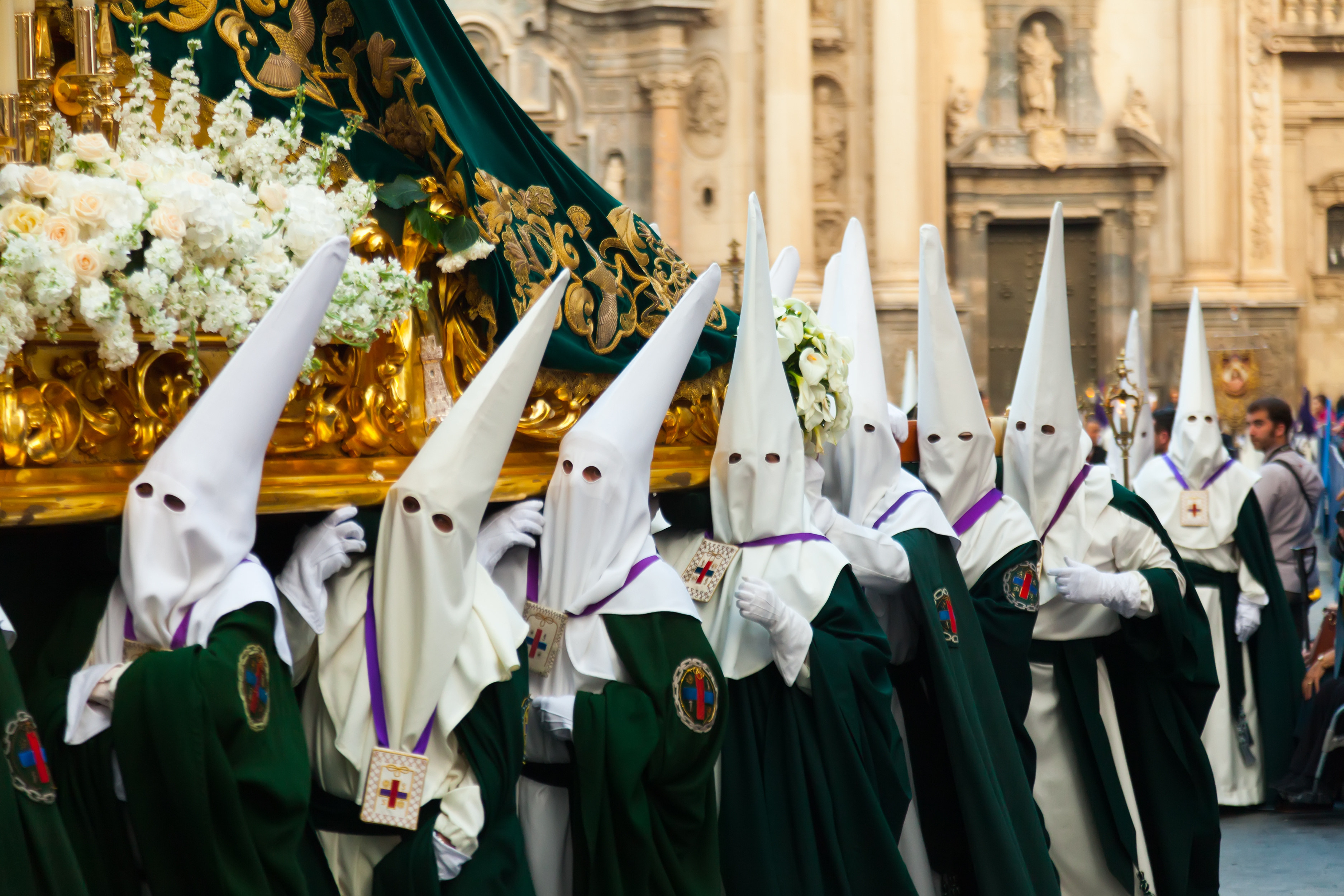 Holy Week procession in Murcia, with nazarenos carrying an ornate flower-covered religious float through the historic city centre.