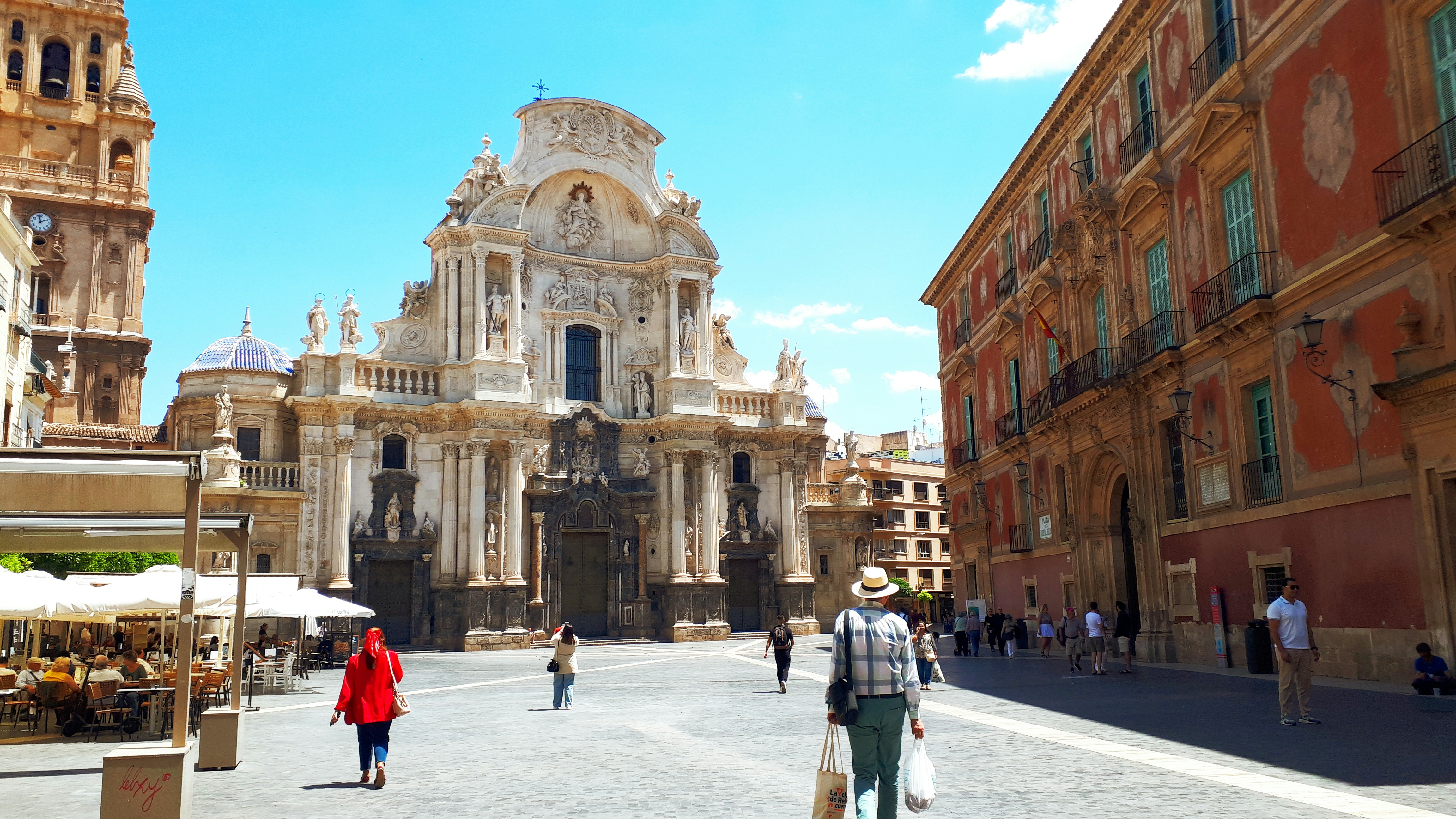 Murcia Cathedral in Plaza del Cardenal Belluga, with people walking across the sunlit square in the Old Town.