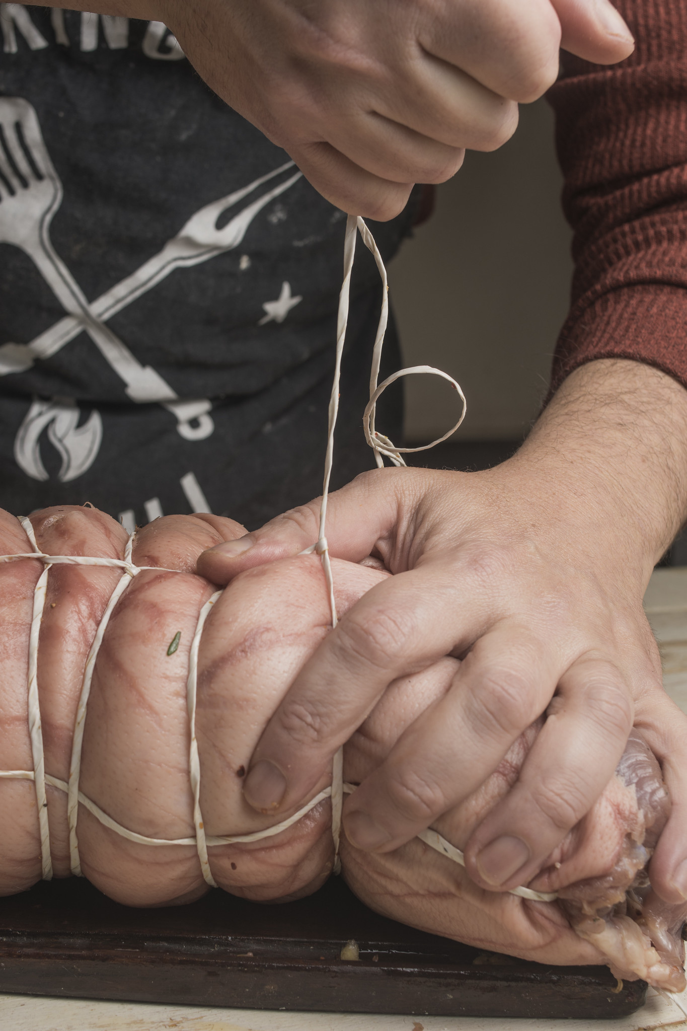 Hands tying rolled porchetta with kitchen string before roasting
