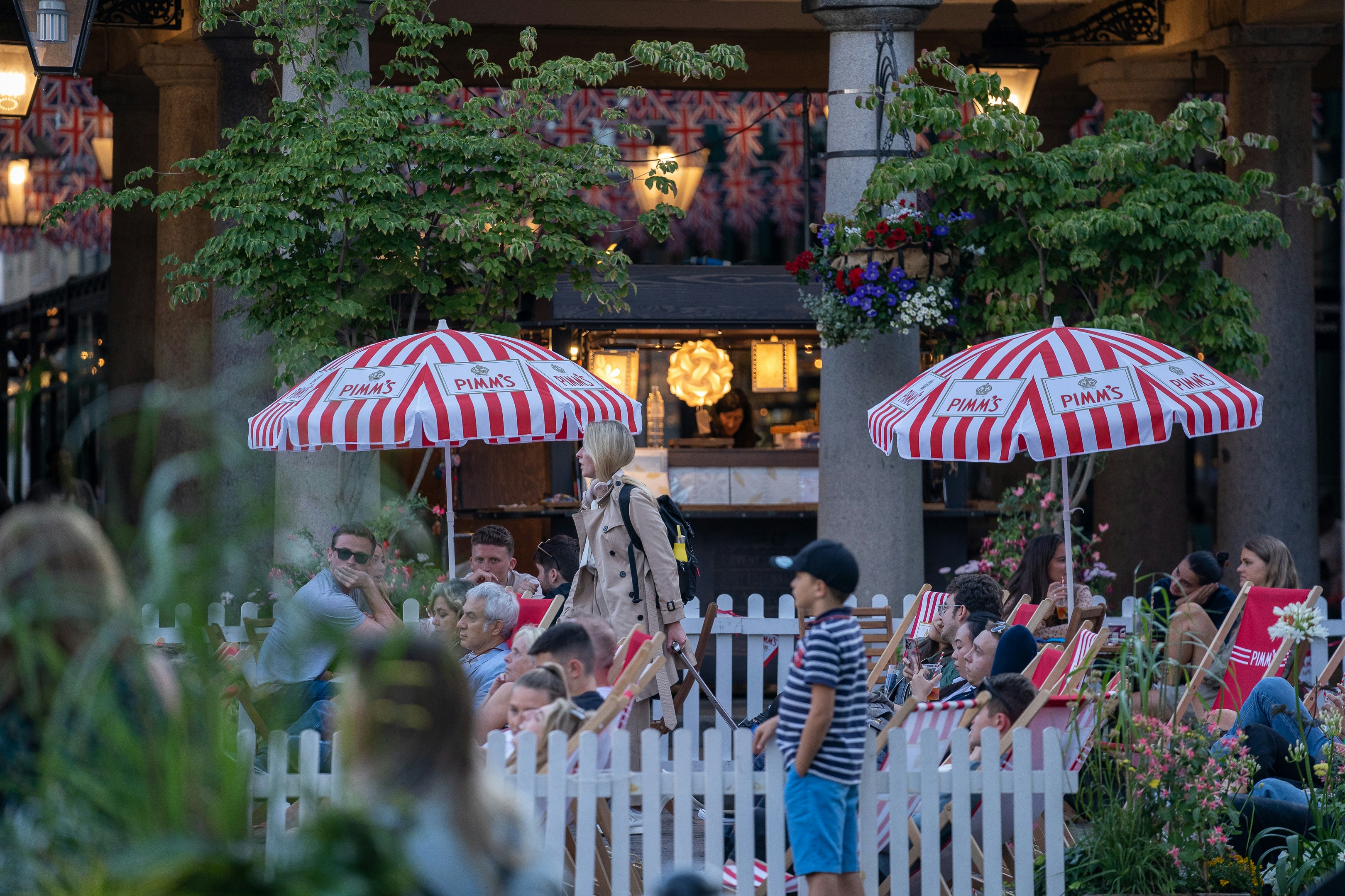 People sitting outside at a London pub terrace with red-and-white Pimm’s umbrellas and deckchairs in summer.
