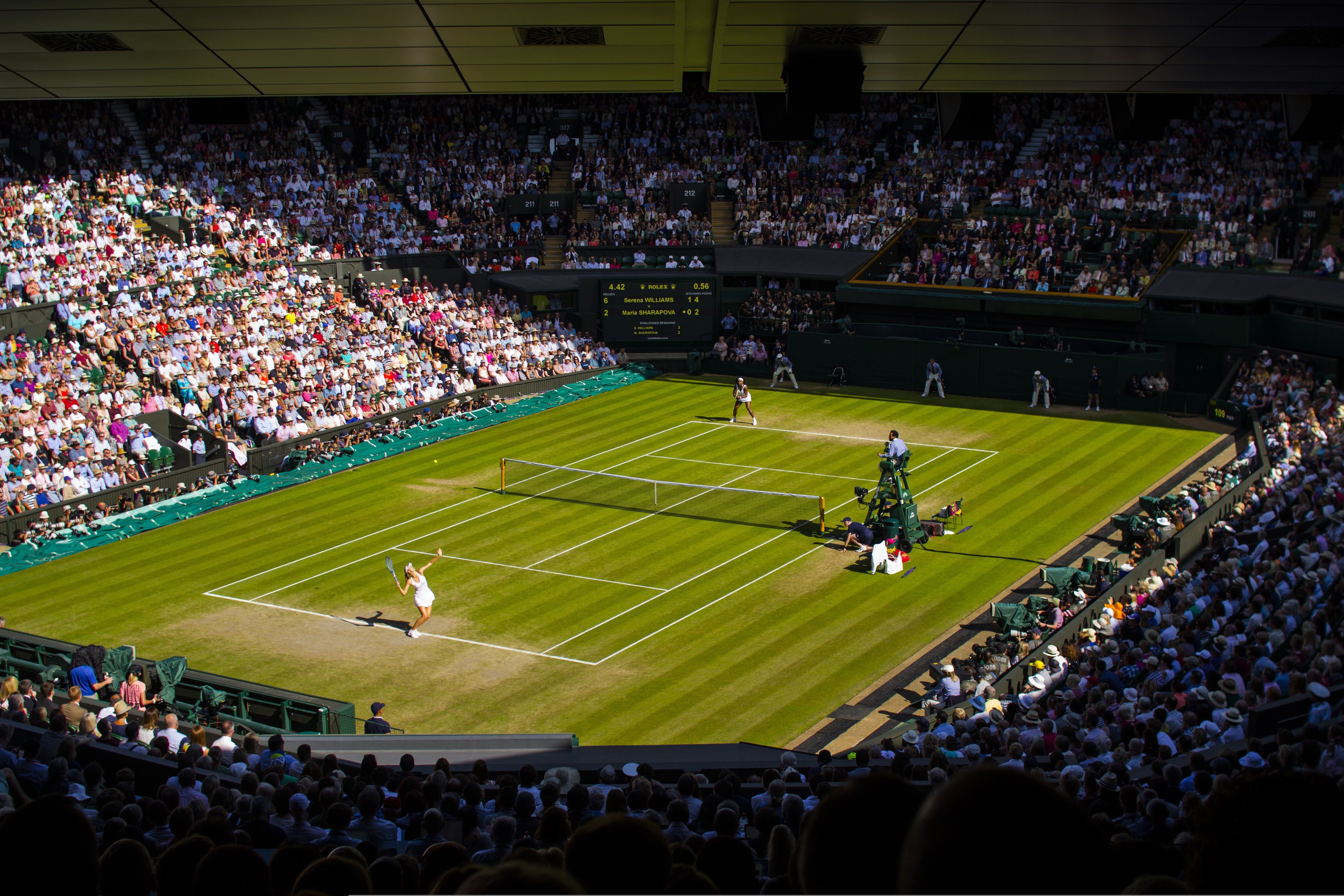 Centre Court at Wimbledon during a tennis match, with spectators filling the stands around the grass court.